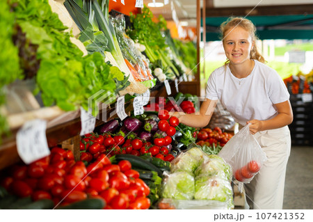 Teenage girl choosing tomato at supermarket 107421352