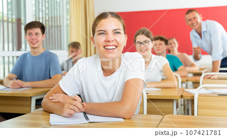 Smiling girl high school student listening to teacher during lesson Smiling girl high school student listening to teacher during lesson 107421781