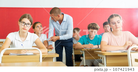 Focused teenage students studying in classroom with teacher 107421943
