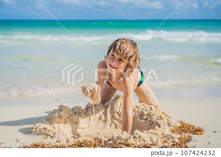 Young boy's pure delight as he explores the sandy playground of the beach, shaping dreams with grains of sand Young boy's pure delight as he explores the sandy playground of the beach, shaping dreams with grains of sand 107424232