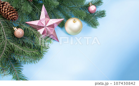 Pink shiny star, balls and cones on pine and spruce branches on blue background with place for text. Christmas, New Year. Copy space 107430842