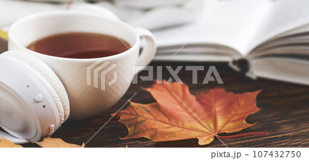 A Cup of hot coffee or tea with autumn leaves and headphones on a brown wooden background A Cup of hot coffee or tea with autumn leaves and headphones on a brown wooden background 107432750