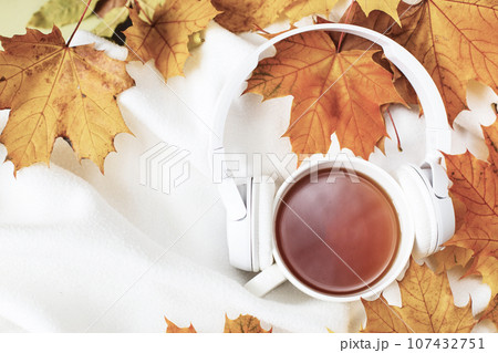 A Cup of hot coffee or tea with autumn leaves and headphones on a knitted white plaid background 107432751