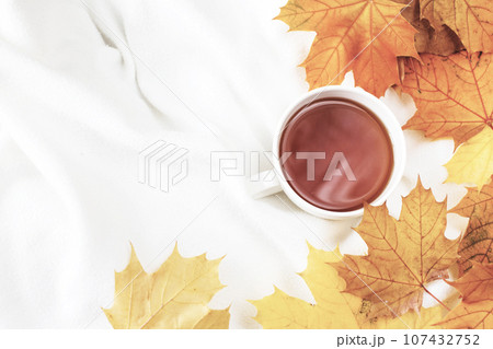 white cup of coffee or tea with golden autumn leaves on a knitted white plaid background .top view. 107432752