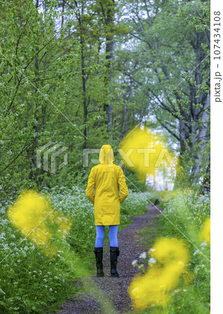 Young woman with yellow raincoat and rubber boots in spring nature 107434108