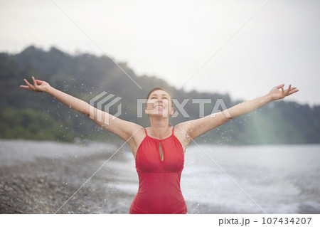 Happy middle aged woman on the beach raised her hands up and enjoys a happy moment. Happy middle aged woman on the beach raised her hands up and enjoys a happy moment. 107434207