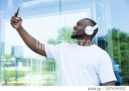 Stylish young African-American man listening to music in headphones with a smartphone in his hands 107434352