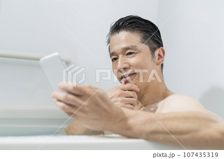 半身浴をしながらスマートフォンで動画を見る40代男性 半身浴をしながらスマートフォンで動画を見る40代男性 107435319