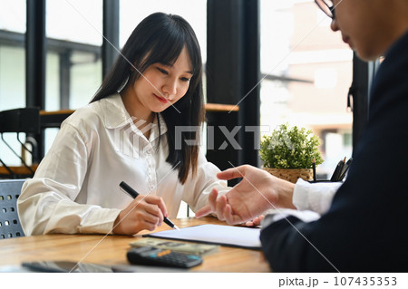 Smiling female client making sale purchase, signing contract with real estate agent. First property purchase and home ownership 107435353