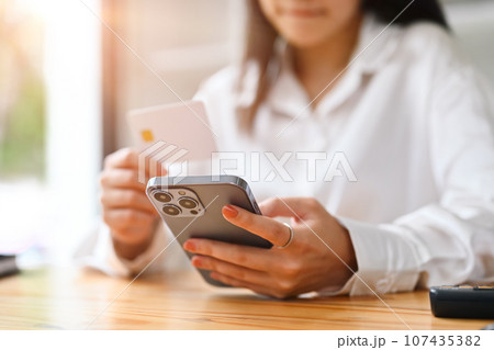 Happy young woman holding credit card and using smart phone, shopping on Internet or payment online 107435382