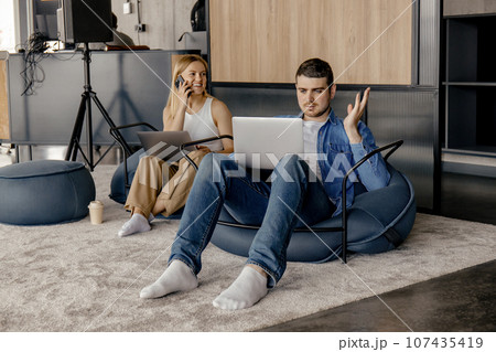 A guy and a girl work on laptops while sitting in comfortable chairs A guy and a girl work on laptops while sitting in comfortable chairs 107435419