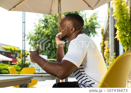 A young African-American man with a smartphone in his hands is sitting at a table 107436673