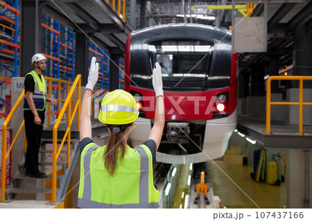 Young caucasian engineer woman or worker signal while engineer man checking electric train. Young caucasian engineer woman or worker signal while engineer man checking electric train. 107437166