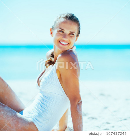 Happy young woman sitting on beach and looking on copy space 107437245