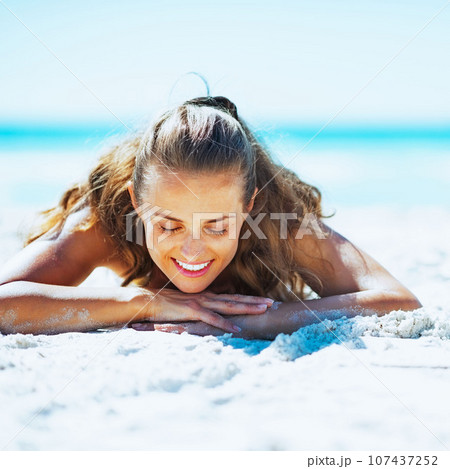 Happy young woman in swimsuit laying on beach Happy young woman in swimsuit laying on beach 107437252