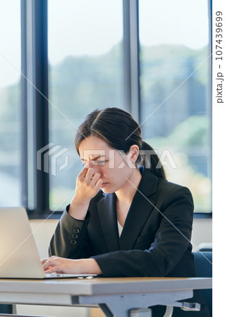 パソコンを操作しながら眉間に手を当てる若い女性 107439699