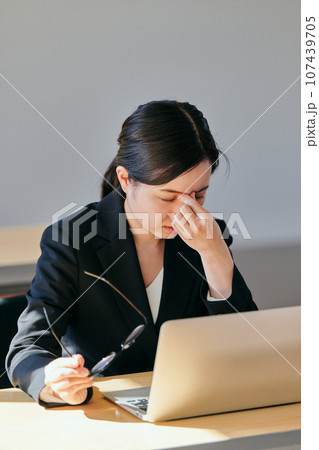 メガネを持ち眉間に手を当てる若い女性 107439705