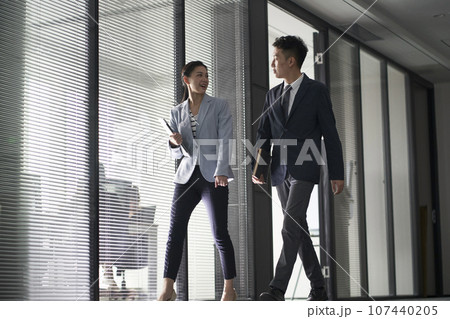 two asian business people on their way to meeting talking while walking in office two asian business people on their way to meeting talking while walking in office 107440205
