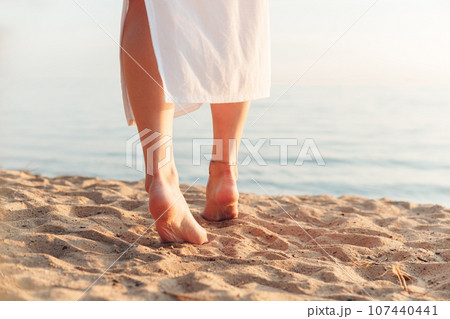 Barefoot woman walking in white dress walking alone on the beach in the sunset Barefoot woman walking in white dress walking alone on the beach in the sunset 107440441