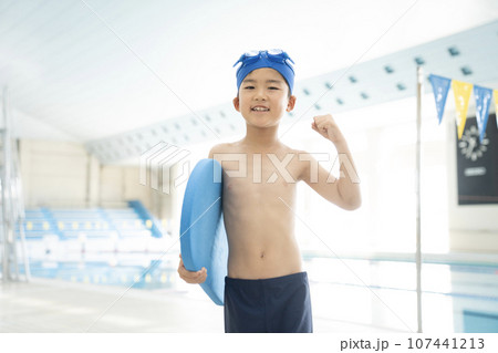 室内プールでビート板を持ってガッツポーズをする少年 107441213