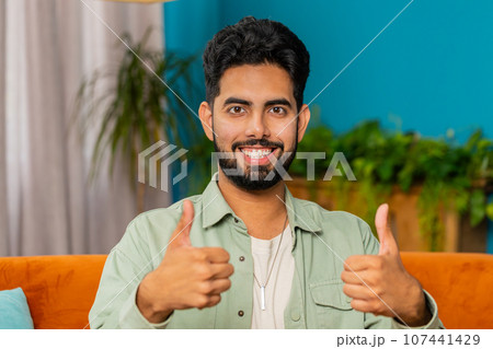 Happy Indian young man looking approvingly at camera show thumbs up like positive sign good news 107441429