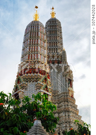 A temple in Thailand with two ornate towers. The towers are decorated with intricate patterns and topped with golden spires. The temple is surrounded by trees and the sky is visible in the background. A temple in Thailand with two ornate towers. The towers are decorated with intricate patterns and topped with golden spires. The temple is surrounded by trees and the sky is visible in the background. 107442028