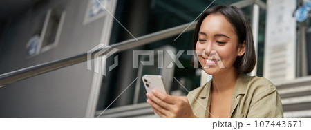 Portrait of asian girl takes selfie on mobile phone. Korean woman smiling, video chat on smartphone app while sits outside on stairs 107443671