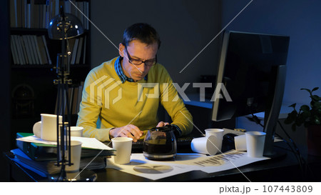 Young busy man typing on computer keyboard while working overtime in night office Young busy man typing on computer keyboard while working overtime in night office 107443809