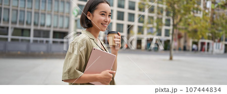 Portrait of asian girl with tablet, drinks coffee on street, walking in city centre 107444834