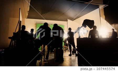 Silhouette images of making of or behind the scenes of video production which produced in the film studio that include all pro light and camera equipment and professional film crew with movie director Silhouette images of making of or behind the scenes of video production which produced in the film studio that include all pro light and camera equipment and professional film crew with movie director 107445574