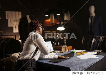 Professional couturier manufacturing business suit bespoken piece, looking online for inspiration. Experienced suitmaker working in exquisite atelier shop, creating premium quality custom made garment Professional couturier manufacturing business suit bespoken piece, looking online for inspiration. Experienced suitmaker working in exquisite atelier shop, creating premium quality custom made garment 107447602