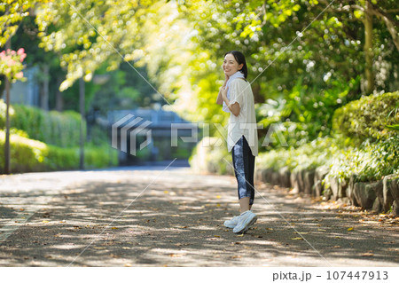 緑の中をスポーツウエアでウオーキングする笑顔の若い女性 緑の中をスポーツウエアでウオーキングする笑顔の若い女性 107447913