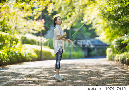 緑の中をスポーツウエアでウオーキングする笑顔の若い女性 緑の中をスポーツウエアでウオーキングする笑顔の若い女性 107447916