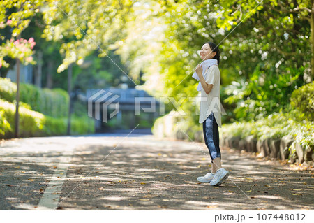 緑の中をスポーツウエアでウオーキングする笑顔の若い女性 107448012
