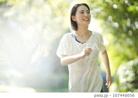 緑の中をスポーツウエアでウオーキングする笑顔の若い女性 107448056
