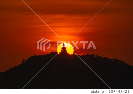 The sun circles in the red sky behind the Big Buddha..Amazing Phuket big Buddha in circle of the sun in red sky..The beauty of the statue fits perfectly with the charming nature. .red sky background 107448421