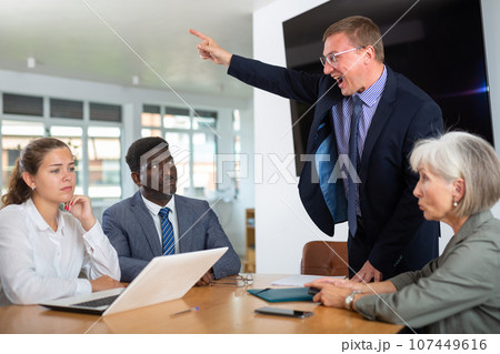 Angry middle-aged man shouting at his business partners sitting around table 107449616