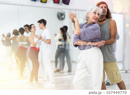 Happy caucasian guy and old lady practising paired latin dance in dance studio 107449770