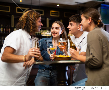 Cheerful adult friends talking and drinking beer at table in pub 107450100