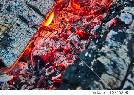 Macro shot of glowing red embers with black charred wood and tiny flames background asset Macro shot of glowing red embers with black charred wood and tiny flames background asset 107452002
