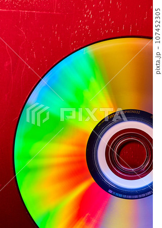 Colorful CD on red background with bursts of rainbow colored lights across silvery surface Colorful CD on red background with bursts of rainbow colored lights across silvery surface 107452305