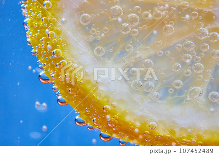 Macro of fizzy bubbles on lemon slice against blue background 107452489