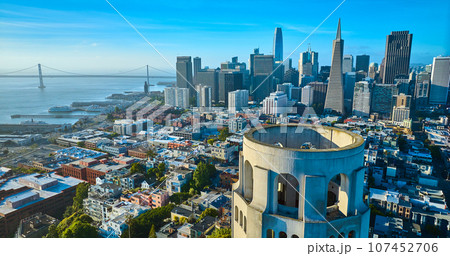 Aerial of roof of Coit Tower overlooking downtown skyscrapers and Oakland Bay Bridge 107452706