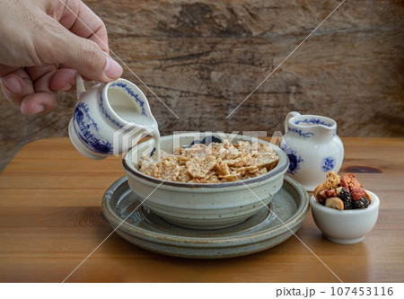 Pouring milk into the Cereal in Ceramic bowl served with Tasty Gadola on wooden table. 107453116