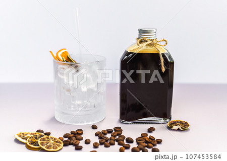 Cold brew coffee in a bottle with transparent glass full of ice on light gray background Cold brew coffee in a bottle with transparent glass full of ice on light gray background 107453584