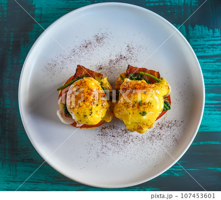 English muffin with poached eggs, bacon and Hollandaise sauce with vegetables 107453601