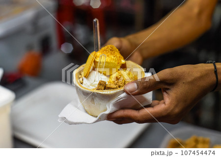 Hand holding coconut and mango ice cream in coconut shell in Jalan Alor street food market in Kuala Lumpur 107454474
