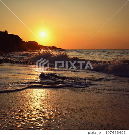 Beautiful sunset on the beach with the sea. Waves on the sea. Greece - Corfu island (Kerkyra) Agios Georgios. A concept for travel, holidays and summer vacations. Beautiful sunset on the beach with the sea. Waves on the sea. Greece - Corfu island (Kerkyra) Agios Georgios. A concept for travel, holidays and summer vacations. 107456491