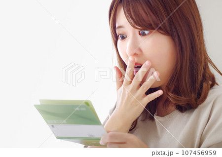 貯金通帳を見て驚きの表情をする若い女性 貯金通帳を見て驚きの表情をする若い女性 107456959