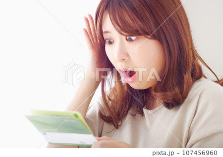 貯金通帳を見て驚きの表情をする若い女性 107456960